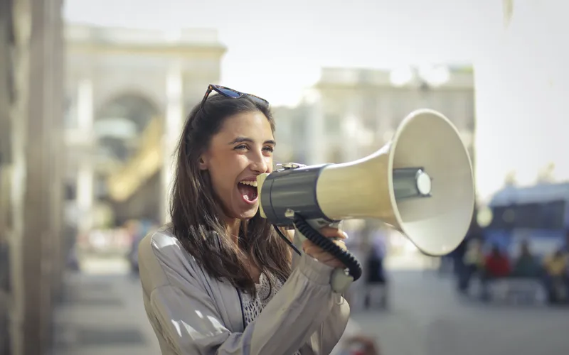Mujer sonriente utilizando un megáfono en una calle concurrida de la ciudad